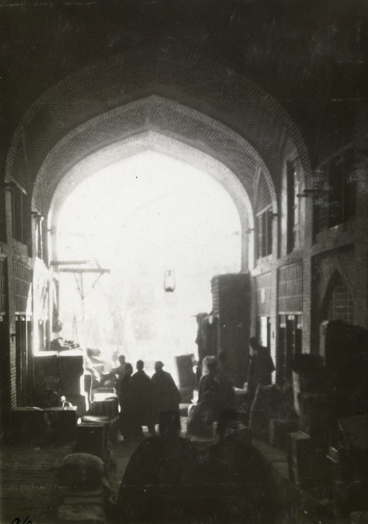 People and stacked goods beneath the high brick arch of a Tehran bazaar.